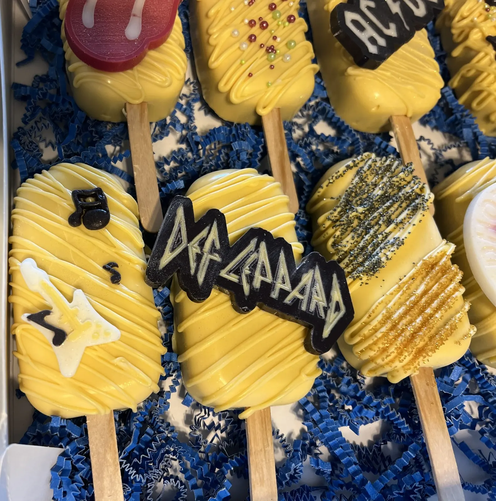 Yellow cakesicles decorated with rock band logos